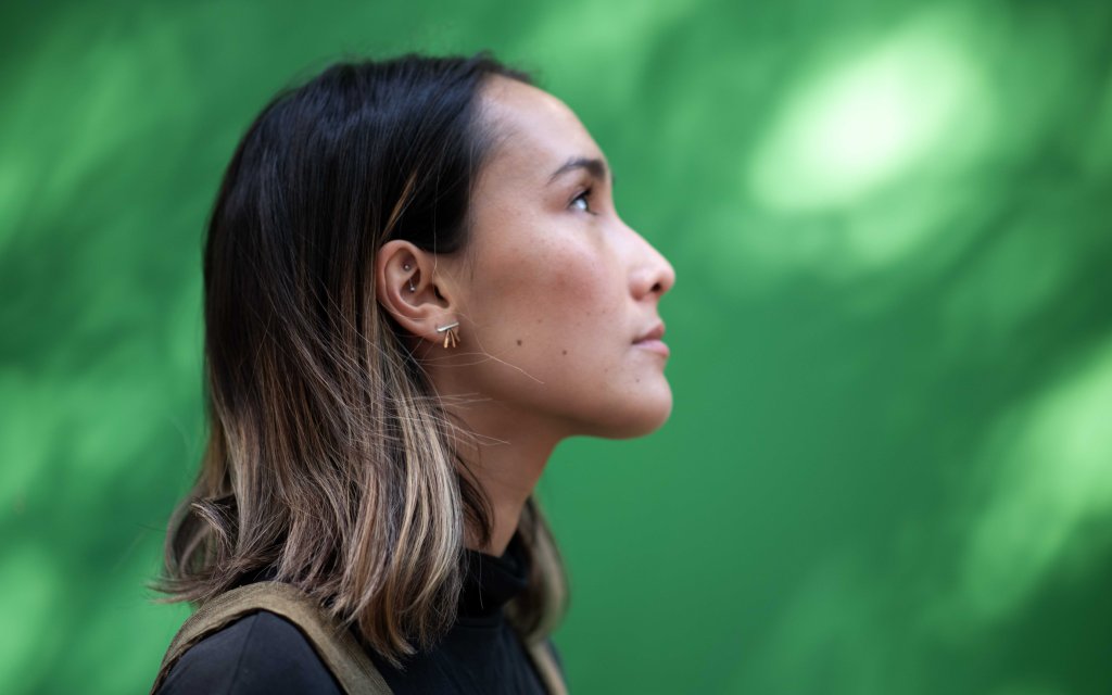 Side profile of a woman with shoulder-length hair, facing right against a blurred green background.